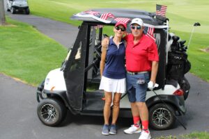 Two golfers pose in front of their cart sporting numerous American flags.