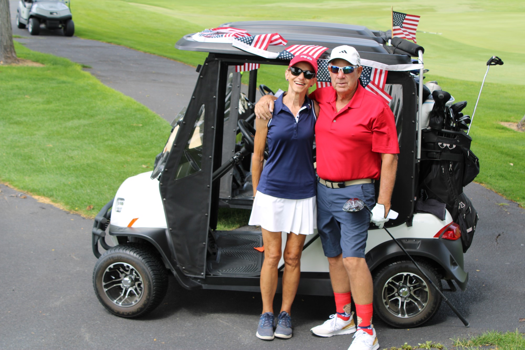 Two golfers pose in front of their cart sporting numerous American flags.