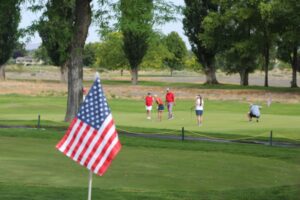 American flag in the foreground with golfers on the green in the background.
